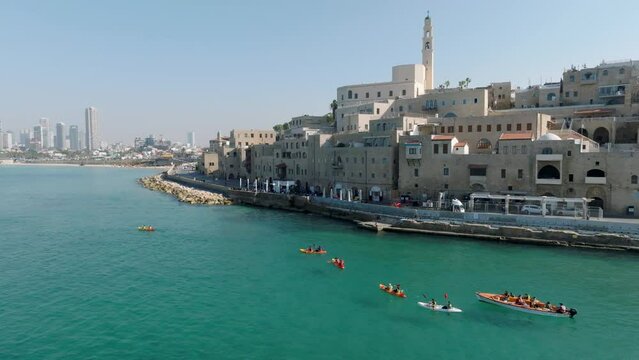 Aerial footage of a group of children paddling kayaks at the exit of the beautiful old port of Jaffa