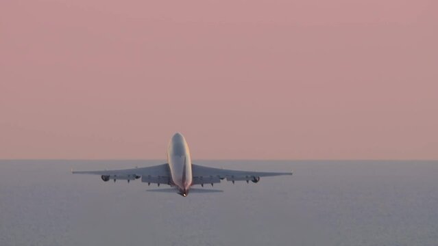 Huge four-engine passenger plane takeoff, sunset pink sky. Jumbo jet departure, rear view. Passenger flight. Flight over the sea