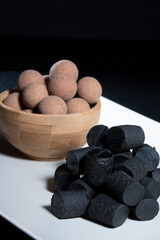 Fototapeta na wymiar Traditional Finnish cuisine: A closeup of the traditional Finnish delicacy of black licorice against a dark background. A bowl of salty liquorice-coated licorice in the background.