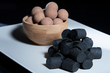 Fototapeta na wymiar Traditional Finnish cuisine: A closeup of the traditional Finnish delicacy of black licorice against a dark background. A bowl of salty liquorice-coated licorice in the background.