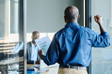 Rear view of young African American economist with financial report knocking on door of director...