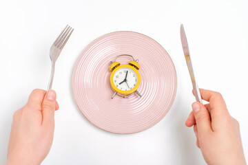 Female hands holding a fork and and knife next to an empty plate on a white background close-up top...