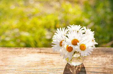 Obraz premium bright sunny background with daisies in a glass on a wooden table top 
