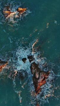 Aerial top view of waves and rocks in the sea. Vertical video