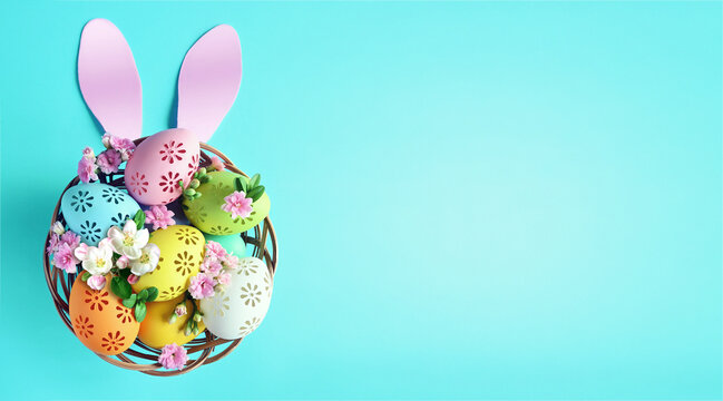 Multi colors Easter eggs in the basket with bunny ears and flowers on blue background. Pastel color Easter eggs.