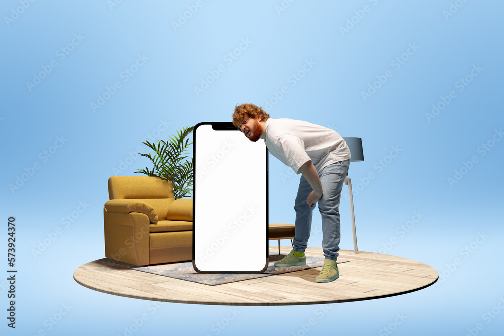 Wall mural Young man leaning on giant 3D model of mobile phone with empty screen for ad, text over blue background with home interior. Online communication, shopping. Mockup for design, logo.