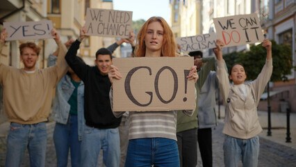 Obraz premium Redhead woman in front shows Go poster protest against racism with students protesting at background