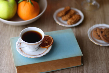 Cup of tea, plates with cookies, glass of orange juice, books, reading glasses, bowl of fruit and candles on the table. Selective focus.