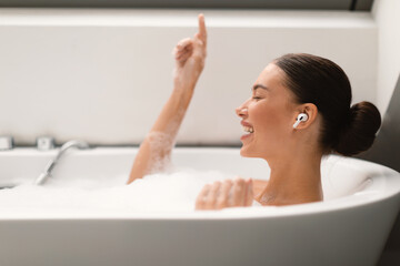 Female Listening Music Wearing Earbuds Relaxing In Bath At Home
