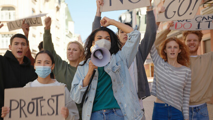 Mixed race protester woman in medical mask shouts slogans into megaphone at protest