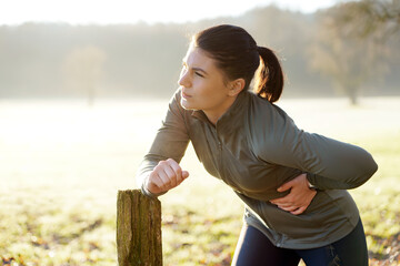 Young woman exercising on a sunny winter morning has pain and side stitch from training and running - 573933508