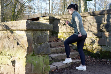 Young athletic woman doing running exercises on old stone stairs on a sunny winter day