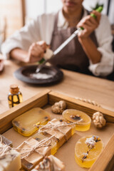 selective focus of wooden tray with herbal soap near african american craftswoman on blurred background.