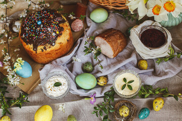 Traditional Easter food. Homemade easter bread, natural dyed easter eggs, ham, beets, butter, cheese on linen napkin on rustic table with spring flowers. Top view.