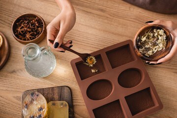 top view of cropped african american woman holding dried herbs near silicone mold and pitcher with liquid soap in craft workshop. © LIGHTFIELD STUDIOS