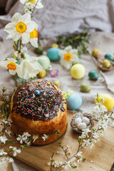 Happy Easter! Homemade easter bread and natural dyed easter eggs with spring flowers on linen napkin on rustic table. Traditional Easter food. Top view
