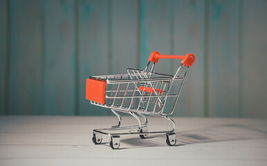 Shopping cart trolley on wood table blue background. Concept e-commerce, marketplace, buy or purchase grocery online store, retail business, consumer empty basket, shipping service, order payment