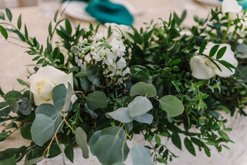 Flower composition with eucalyptus leaves and candles in the center of the table. Wedding set up, dinner table reception. A plate with a green cloth towel. Decor closeup.