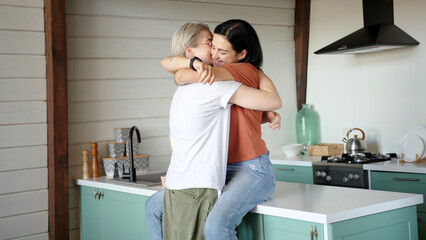 Brunette in orange t-shirt hugs and kisses blonde girlfriend