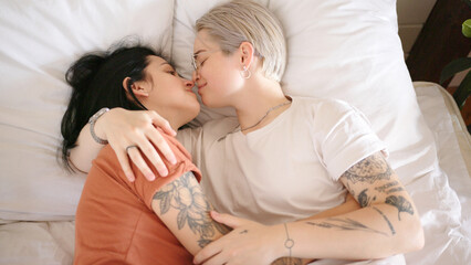 Romantic lesbian couple with tattoos kisses lying on bed