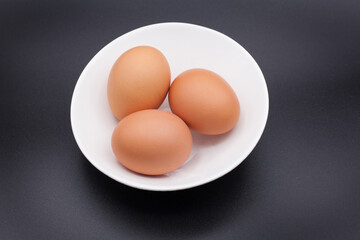 Three chicken eggs in a white bowl against a black background