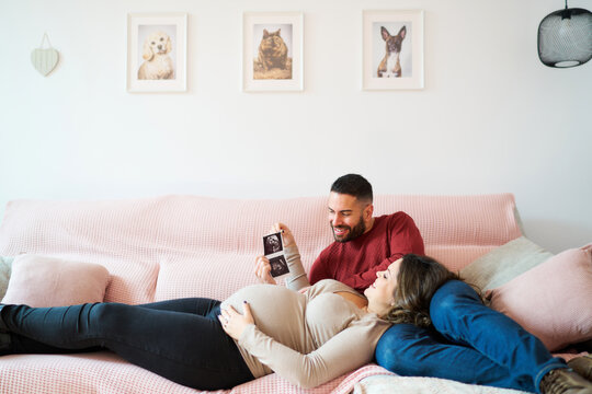 Smiling pregnant couple looking at ultrasound at home