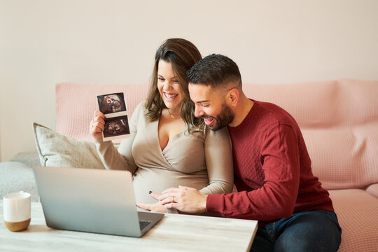 Happy couple with laptop and photo of ultrasound