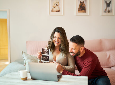 Happy couple with laptop and photo of ultrasound