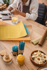 dried camomiles and homemade candles near wax sheets and cropped african american craftswoman on blurred background.