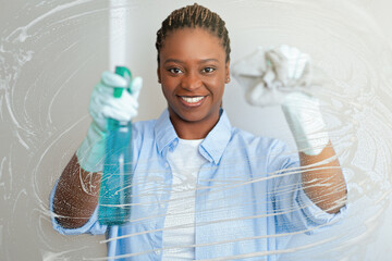 Cheerful funny african american lady cleaning windows at home