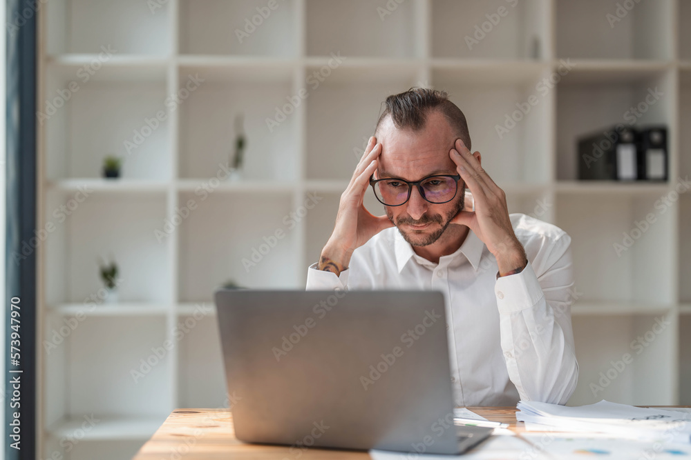 Wall mural young unhappy man office worker feeling bored at work, looking at laptop with demotivated face expre