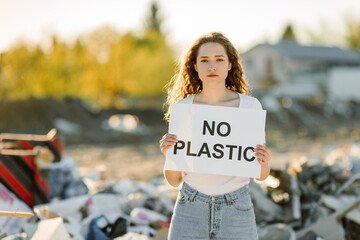 Young woman holding no plastic sign on trash place