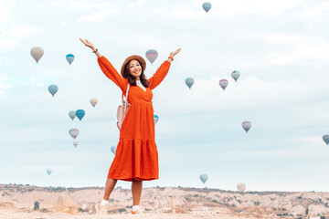 Girl stood amidst the orange rocks of Cappadocia watching dreamily as the balloons floated away towards the horizon, the sun highlighting her gentle figure and the red dress she was wearing.