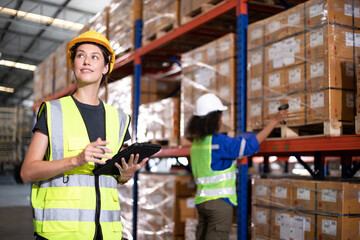 Female supervisor talking about job with worker in warehouse and they compares checklist with cardboard and barcode scan in store.