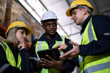 Male and Female workers wearing helmets and using tablet in logistics distribution warehouse. Group of diversity warehouse worker meeting and checking list inventory in industry factory.
