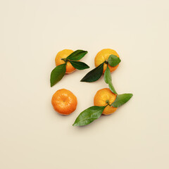 Ripe fresh orange yellow tangerines with green leaves on beige table background, minimal square pattern. Citrus fruits mandarines as trend food composition flat lay minimal, still life photo