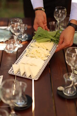 a person holding a plate of cheese and greens in front of a table with wine glasses