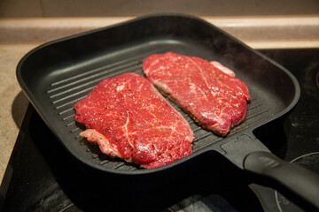 Raw minute steak of marbled beef in a grill pan on an electric cooking surface
