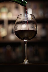 a wine glass with a red wine in it is being filled with wine from a bottle into a wine glass