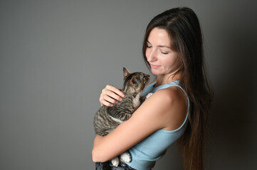 Obraz premium Woman hugging her kitten. Striped kitten lies on on the shoulder of a woman on gray background.