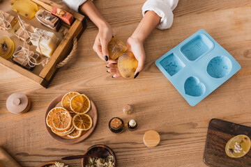 top view of cropped african american woman holding herbal soap near natural ingredients and silicone mold on wooden table.