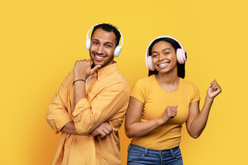 Obraz premium Cheerful young african american guy and woman in wireless headphones dancing, have fun together