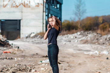 Sexy curly woman is talking on a mobile phone. Black T-shirt and jeans. Blurred background.