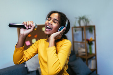 Cute preteen black girl  holding microphon singing karaoke at home, recording songs for contest.