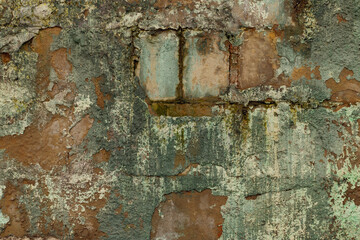 Close-up of a brick wall with cracks, stains and mold. Plaster is peeling of mostly.