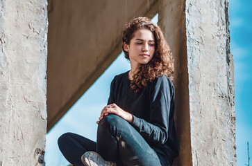 Curly cute young woman sitting in the window of an unfinished house. Architecture, construction.