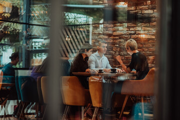 Photo through the glass of a group of business people sitting in a cafe and discussing business plans and ideas for new online commercial services