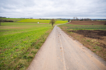 Agricultural path between multiple agricultural fields, stacked straw bale in the distance, cloudy...