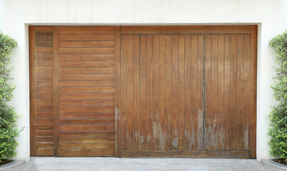 Large wooden gate on cement wall decorated with green tree.
