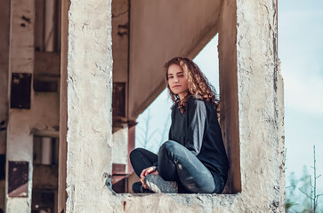Curly cute young woman sitting in the window of an unfinished house. Architecture, construction.